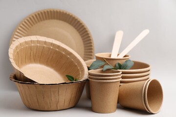 Set of disposable tableware and green leaves on light grey background, closeup
