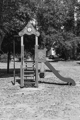 A black and white photo of a playground slide evokes a sense of quiet nostalgia. The play equipment stands still under the midday sun, highlighting its intricate structure and peaceful solitude.

