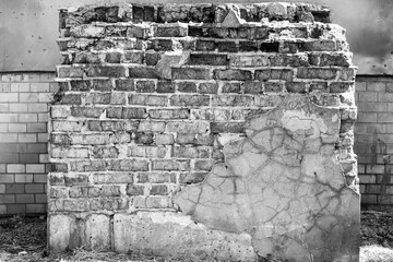 A weathered, crumbling brick wall with exposed concrete and peeling plaster, presented in a stark black and white, highlighting urban decay and texture.

