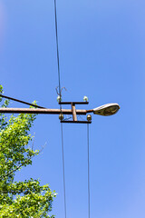 An old street lamp and power lines against a clear blue sky. The image captures the contrast between rusty, vintage utility infrastructure and a bright, modern day.

