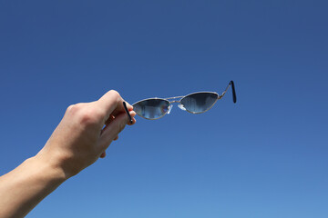 Woman holding stylish sunglasses against blue sky, closeup