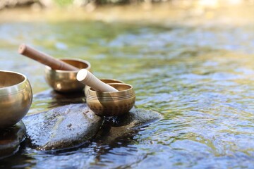 Obraz premium Tibetan singing bowls with mallets on stones in river, closeup. Space for text