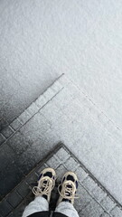 Top view of first snow on steps and asphalt, feet in sneakers, winter morning outdoors