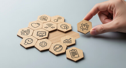 Photo of a hand places a hexagonal wooden tile with a gear and clock icon into a cluster of similar tiles representing business concepts