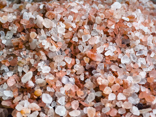 Pink Himalayan salt crystals in varying sizes displayed on a textured surface for culinary and health uses