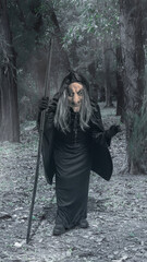 Old witch woman walking through the forest with a stick. The scene is scary and creepy. Concept of...