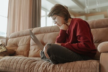 A young woman works on her laptop in a cozy living room, capturing the modern freelance lifestyle....