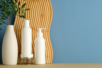 White bottles and glass jar with white lid, vase with green leaves, wavy panel, blue background, clean cosmetic branding.