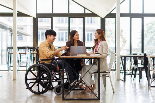 Asian Male Manager On A Wheelchair Sitting With His Colleagues At Workplace