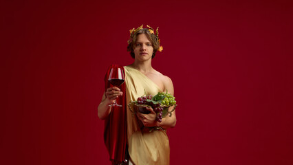 Young man in toga holding grapes and red wine glass on festive background. Concept of vineyard...