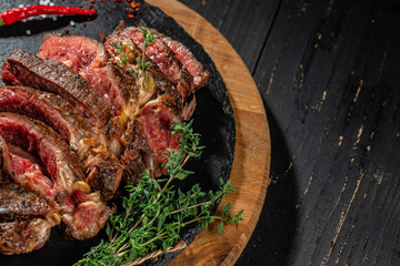 Close up of sliced grilled tomahawk steak with herbs on wooden board, top view, copy space
