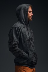 Man in dark hoodie poses against black background, showcasing modern fashion and personal style in an artistic setting