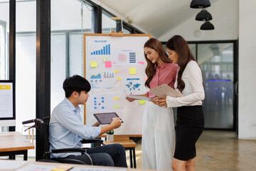 Fototapeta premium Happy business man on wheelchair and her female colleague cooperating while working on paperwork in the office. 