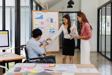 Happy business man on wheelchair and her female colleague cooperating while working on paperwork in the office.

