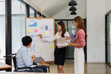 Happy business man on wheelchair and her female colleague cooperating while working on paperwork in the office.
