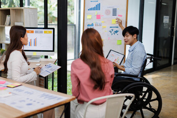 Obraz premium Happy business man on wheelchair and her female colleague cooperating while working on paperwork in the office. 