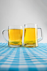 Beer mugs with a blue checkered tablecloth or napkin on a white table. Concept of Oktoberfest. Bavarian German culture festival decoration symbol