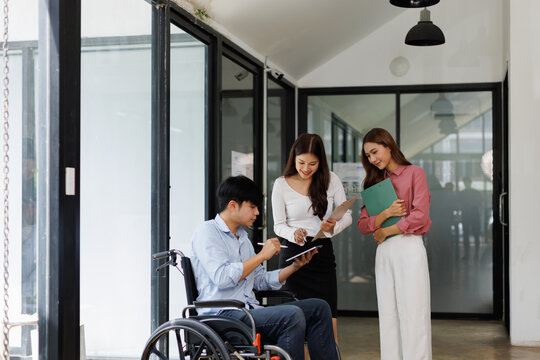 Group shot of diverse business people, disabled asian man on wheelchair chatting with colleagues together at meeting room at office
