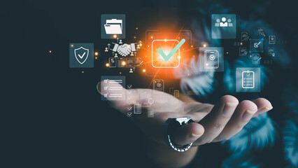 Hand presenting glowing checkmark icon surrounded by business, security, and document holographic symbols on dark background. Concept of digital verification and successful completion.