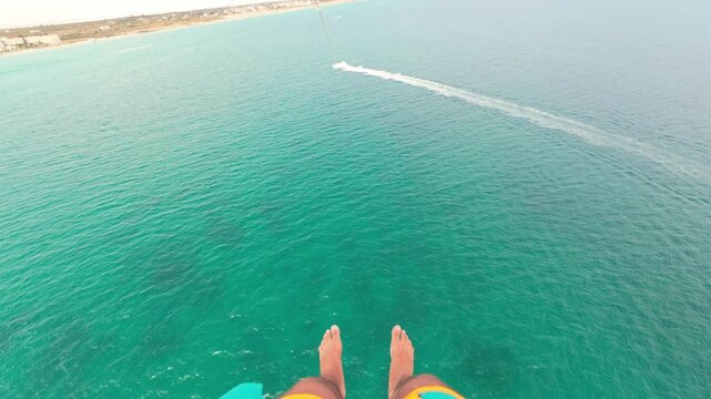 First Person parasailing. Legs above the seawater while parasailing. A boat pulling a parasailing couple.