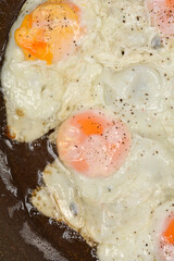 A close-up shot of multiple fried eggs with sprinkled pepper sizzling in a pan