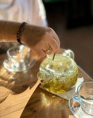 Close-up of a male hand with a wedding ring stirring tea leaves in hot water inside a transparent...