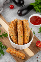 Baked crispy eggplant sticks served with tomatoes sauce in a white ceramic bowl on a gray concrete background. Vegetarian healthy dish. Selective focus
