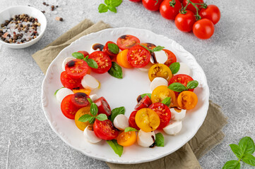 Caprese salad with cherry tomatoes, mini mozzarella and fresh basil with balsamic vinegar in a white plate. Healthy vegetarian meal.