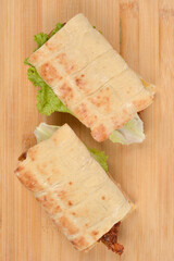 A top-down shot of two flatbread sandwiches with a hamburger patty and vegetables on a wooden cutting board