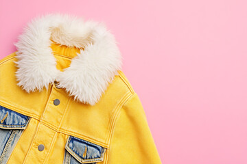 A fashionable yellow denim jacket with a fluffy white collar on a pink background, highlighting its trendy design and stylish appeal