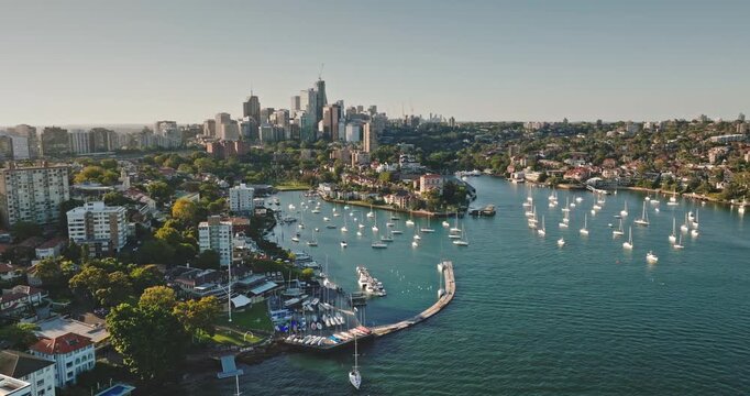 Australia, Sydney: Sydney's modern city skyline above Rushcutters Bay, featuring boats sailing in marina and sunlit residential buildings skyscrapers. Aerial view drone flight footage panorama
