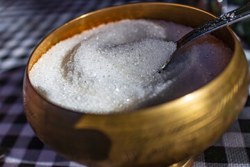 A golden bowl filled with sugar sparkles under soft light. A spoon rests inside, catching the light