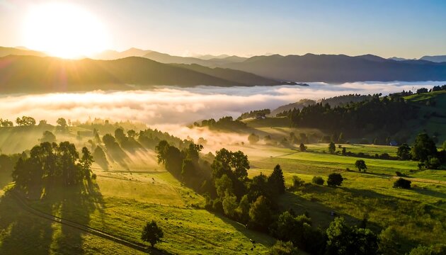 A vibrant, sunrise over a misty valley reveals rolling hills, trees, and mountains silhouetted in the distance. Rays of sunlight illuminate the landscape