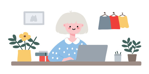 A stylish woman is seated at a desk, engrossed in work on her laptop, with a room for creativity and work. A picture of a shirt, plants in pots and clothes hanging are arranged on the desk. 