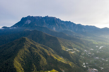 Aerial view of Mount Kinabalu surrounded by lush green hills and valleys in Sabah, Malaysia. Scenic landscape of the highest mountain in Southeast Asia under clear sky.