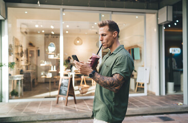 Man strolling with drink and phone, immersed in mobile feed—illustrates mobile-first urban workflow, tech connectivity, and digital presence in motion.