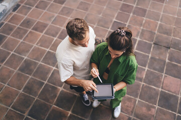 Focused creative duo standing close with tablet and stylus, visually interpreting design solutions, embracing smart collaboration and shared responsibility in tech creation.