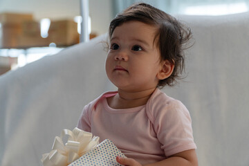 Healthy little cute daughter holding gift box ribbon looking at family sitting in bedroom. Lovely...