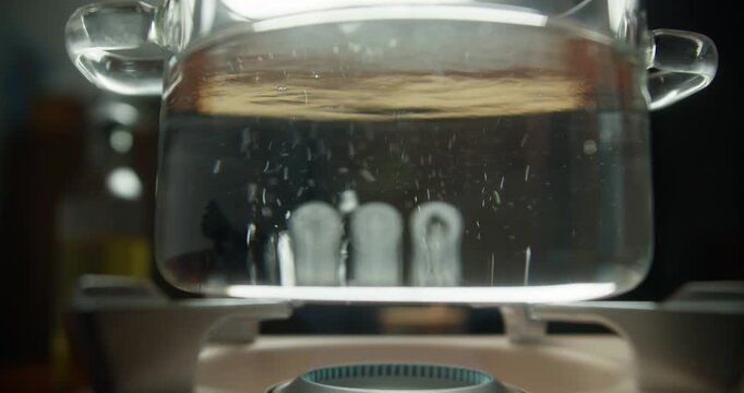 Boiling water in a transparent pan on a gas stove. Filmed in RAW format. High-quality 4K video.
