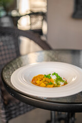 Bowl of curry with rice and peas served on a glass table in a cozy indoor setting. Garnished with herbs, ideal for restaurant, home-cooked, or food blog themes