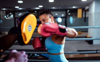 Fototapeta premium Female boxer training in boxing ring with male trainer at gym.