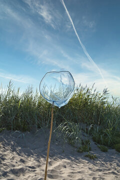 Blue landing net with wooden pole on a sandy beach, with a blue sky. Vacation
