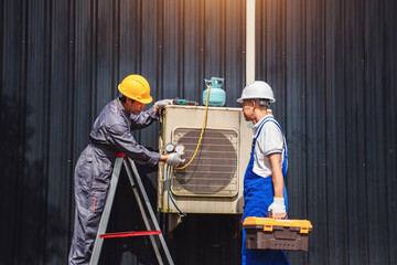 Technicians Inspecting Air Conditioning Unit on Building Wall during Daytime in Industrial Setting with Safety Gear and Tools