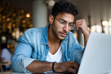 Young Indian entrepreneur working on laptop in cafÃ©, digital startup lifestyle, 