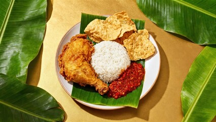A plate of flavorful fried chicken, rice, and spicy sambal, presented beautifully on a bed of...
