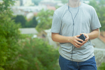 Male walking outside in casual wear with earphones and mobile phone in hands. Concept of mindfulness, relaxation, peaceful outdoor routine and conscious living. Daily balance of technology and nature.