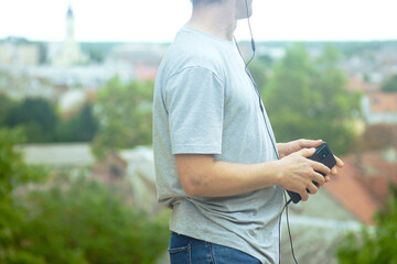 Tourist man holding smartphone with headphones while exploring city. Concept of audio guide travel, self-guided walking tour and independent sightseeing. Urban adventure with digital navigation 