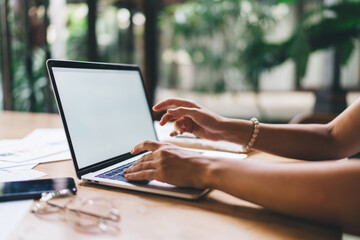 Obraz premium Close-up of hands using laptop with glasses and smartphone nearby, working efficiently in quiet modern environment with focus on productivity.