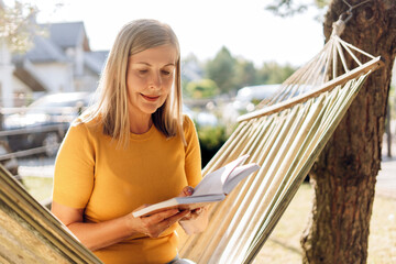 Senior woman reading book while relaxing in hammock in garden