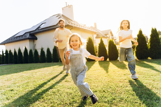 Happy family running in the garden of their house with solar panels